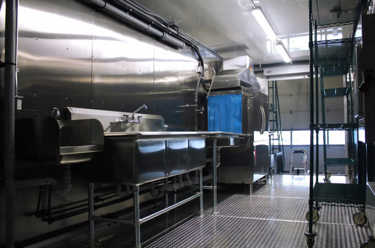 Interior of mobile dishwashing trailer.  Stainless steel sink with an industrial dishwasher.